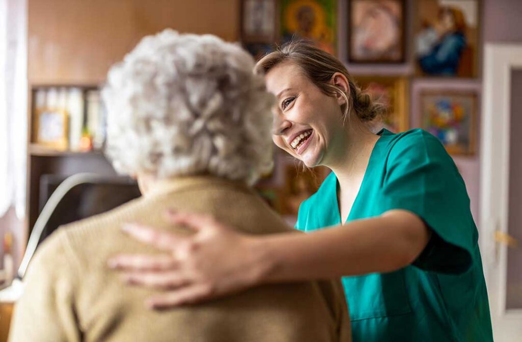 Three older adults conversing and smiling together in a cozy, well-lit assisted living common room.