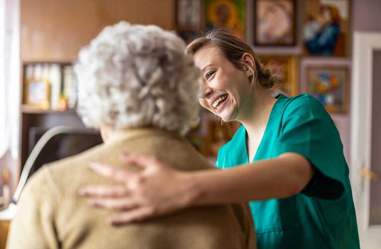 Three older adults conversing and smiling together in a cozy, well-lit assisted living common room.